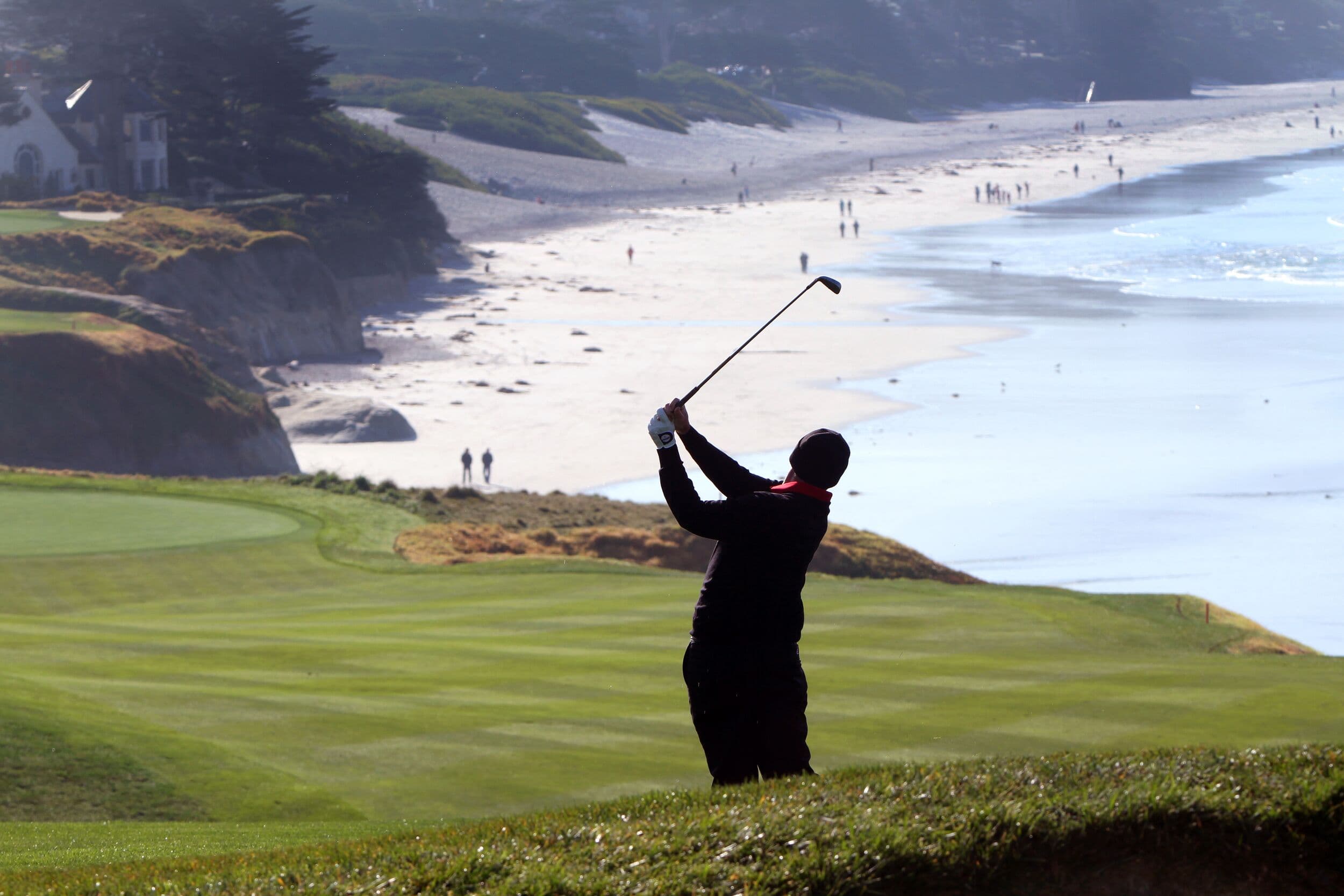 Golfer playing approach on Hole 9 fairway at Pebble Beach Golf Links® — Stillwater Cove beach stretching behind